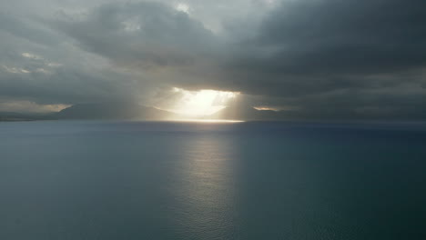 rayos de sol que pasan sobre nubes oscuras sobre el mar en calma en la costa de castellammare del golfo en trapani, sicilia, italia