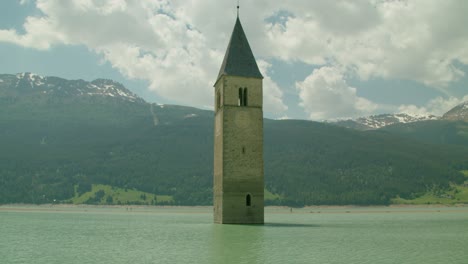 Full-shot,-Scenic-view-of-Kirchturm-von-Altgraun-clock-tower-near-the-shore-in-Italy,-People-walking-in-the-background