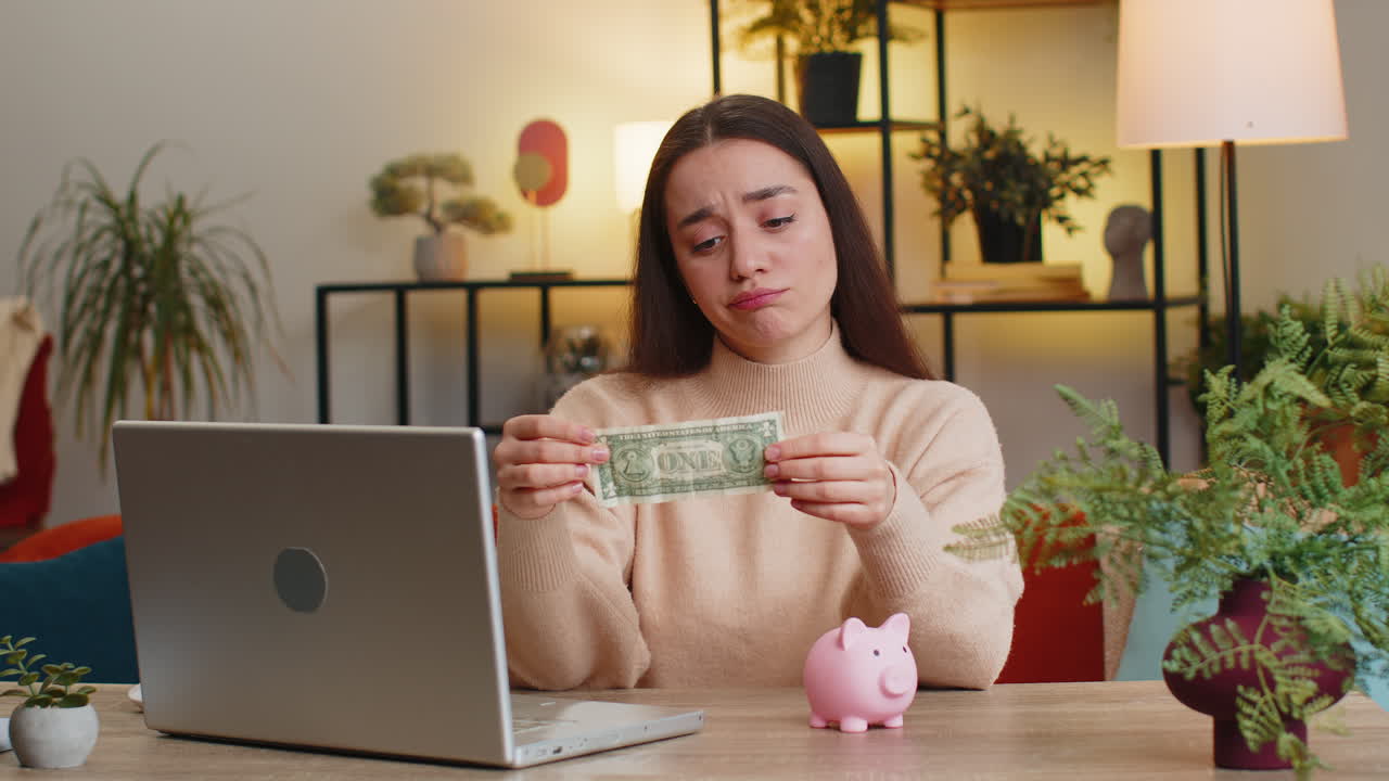 Poor caucasian young woman holding piggybank and one dollar insufficient amount of money poverty