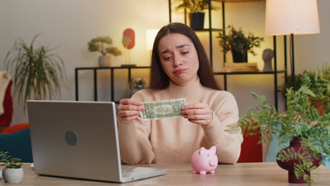 poor caucasian young woman holding piggybank and one dollar insufficient amount of money poverty