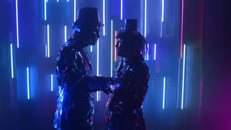 two robot dancers in glittering costumes dance against a neon wall.