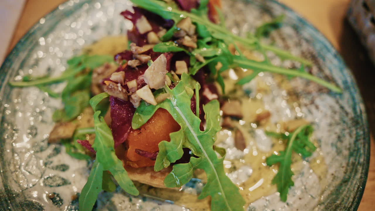 Nærbillede af en gourmet-appetizer toppet med friske grøntsager, nødder og sauce, serveret på en keramisk tallerken