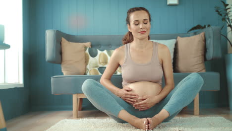 Closeup-smiling-expectant-mother-holding-belly-in-yoga-pose-at-home.