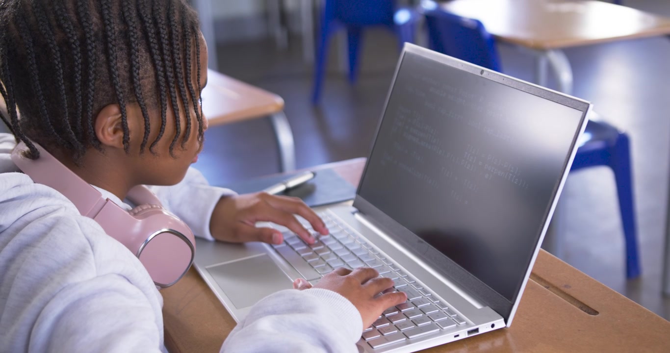 Adolescente maschio afroamericano che si avvicina da sinistra, che digita su un laptop argentato a scuola per i compiti
