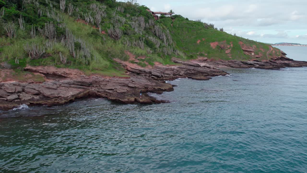 Nostalgic aerial orbit of a single person watching and enjoying the sea on the shore of Tartaruga beach, B&uacute;zios, Brazil