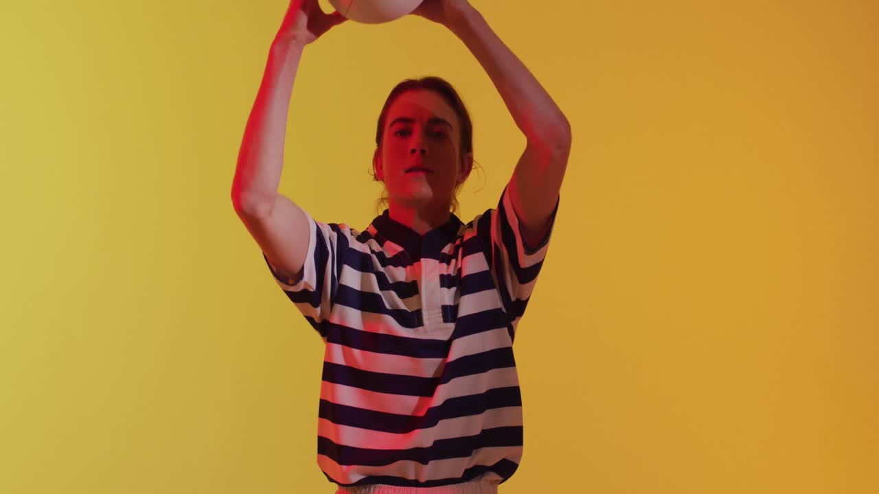 retrato de una jugadora de rugby caucásica con una pelota de rugby sobre iluminación amarilla de neón