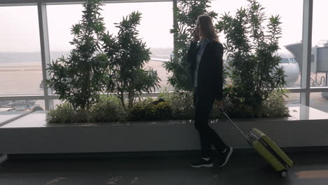 mujer con maleta hablando por teléfono y caminando en la terminal del aeropuerto