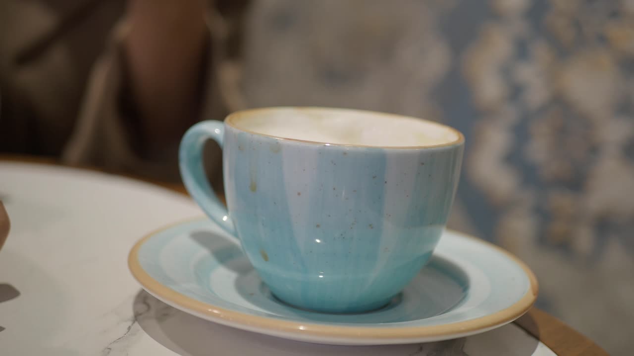 Una mano che prende una tazza da caffè in ceramica blu da un piattino