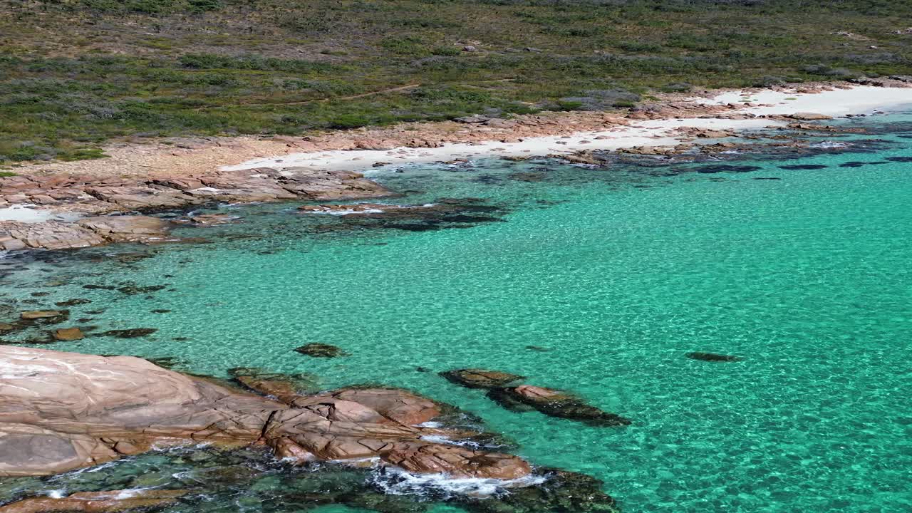 Serene drone shot of a Western Australian coastline with calm turquoise water and rocky cliff at midday.