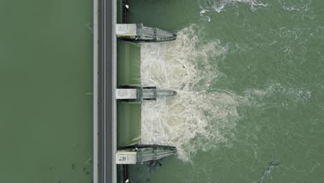 Aerial:-top-down-view-of-dam-releasing-water,-water-discharge-downstream