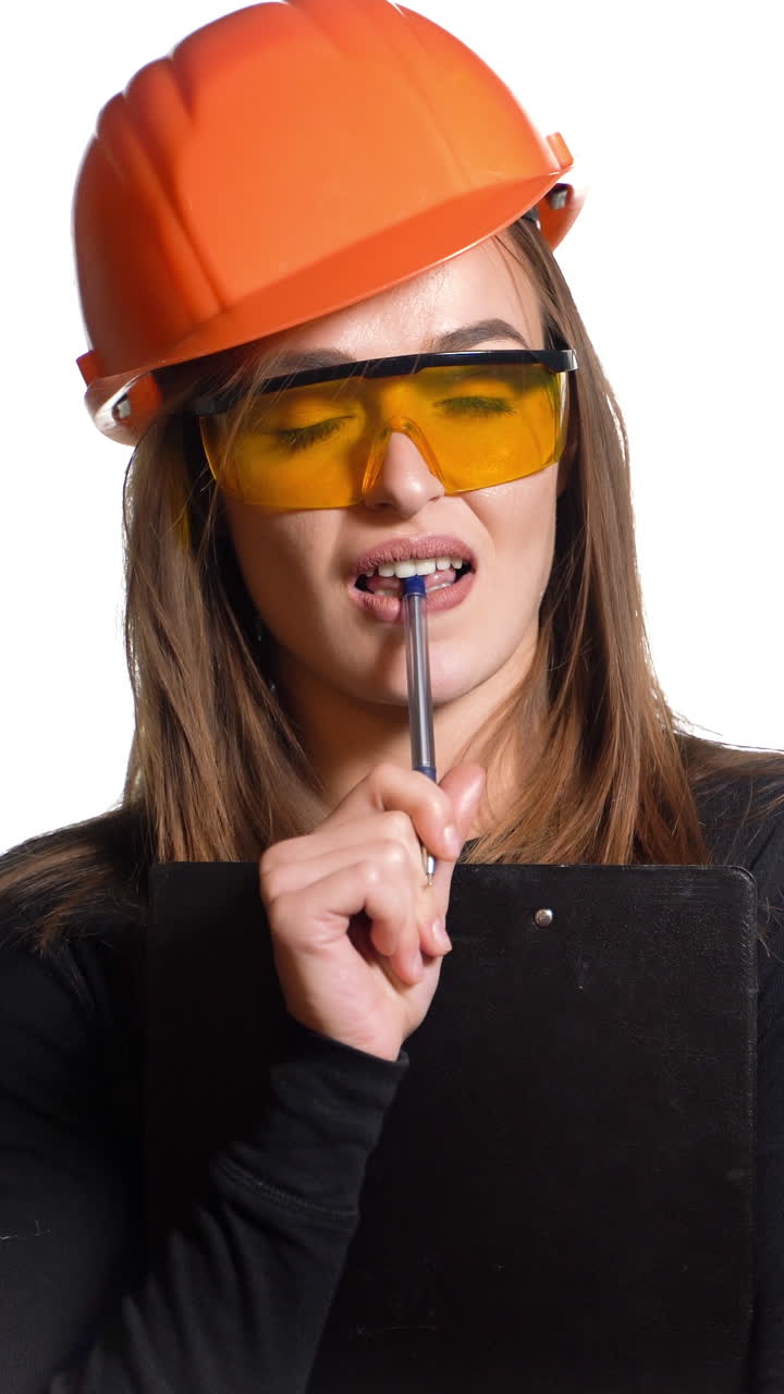 Young woman construction worker in hard hat on a white background. Attractive woman builder with notepad in hand makes the decision Vertical video