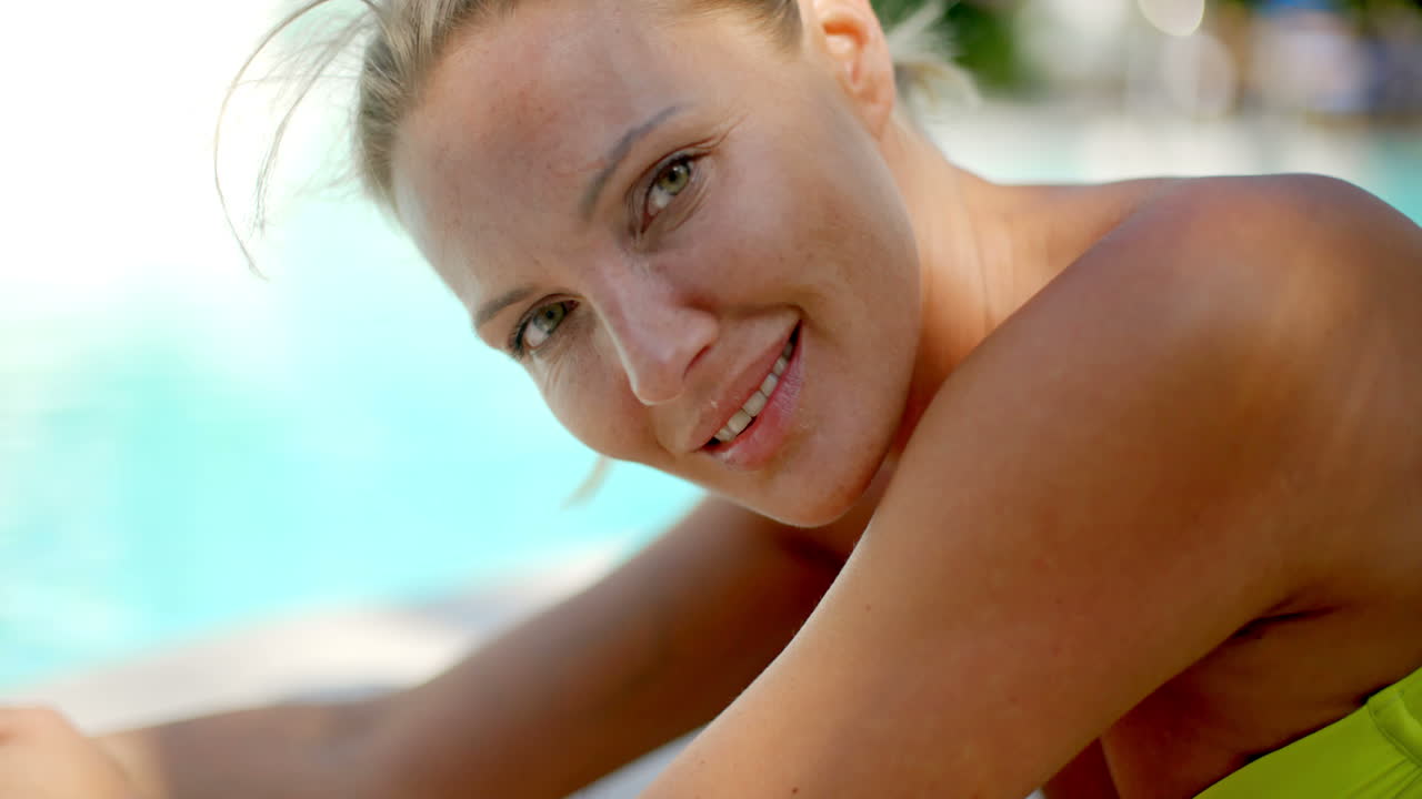 Donna bionda che sorride alla telecamera a bordo piscina