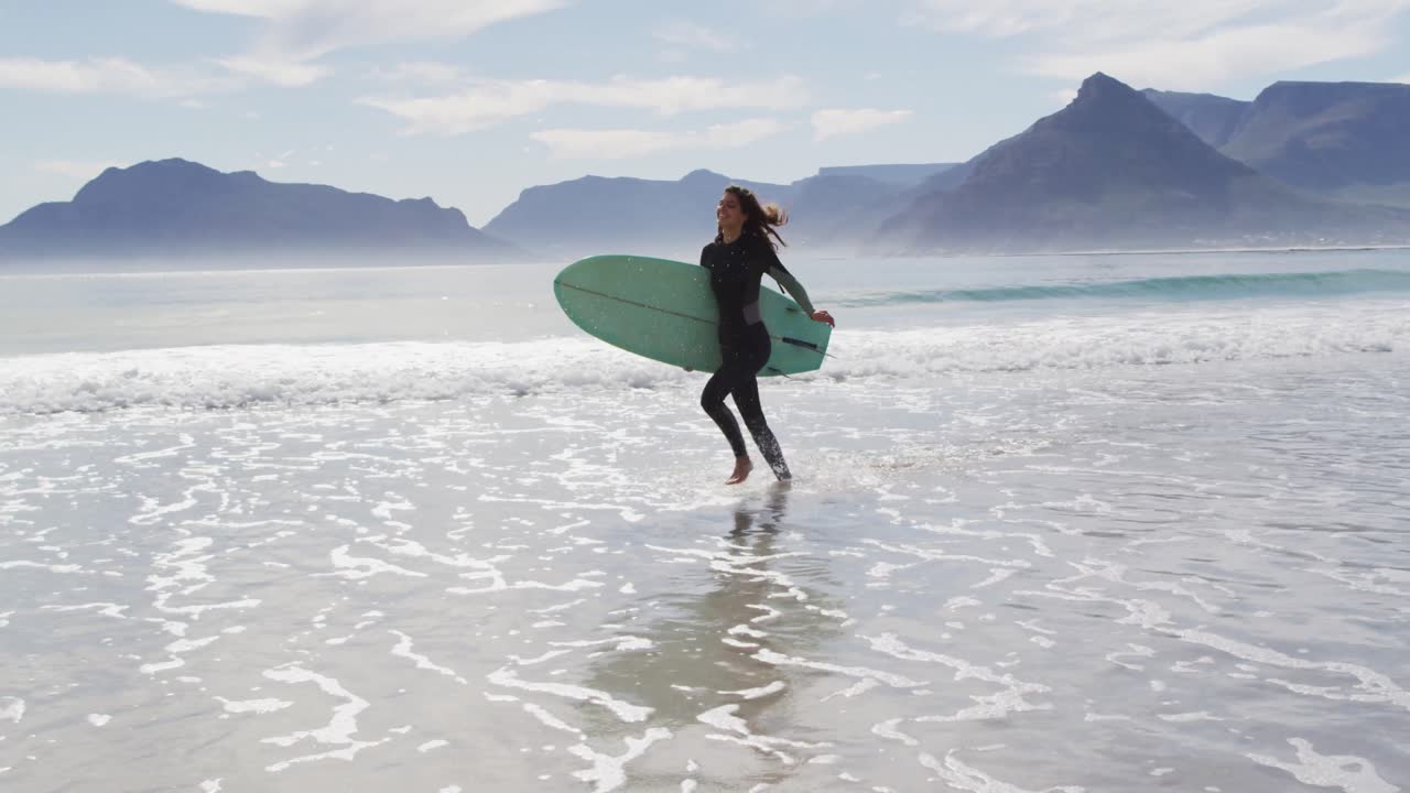 해변에서 서핑 보드를 들고 달리는 행복한 혼합 인종 여성