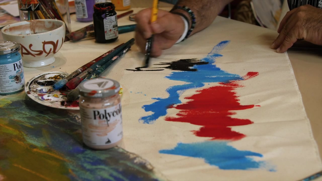 Vista frontale di un artista che crea un dipinto astratto con un pennello su tela, circondato da barattoli di vernice e materiali artistici in uno studio creativo.