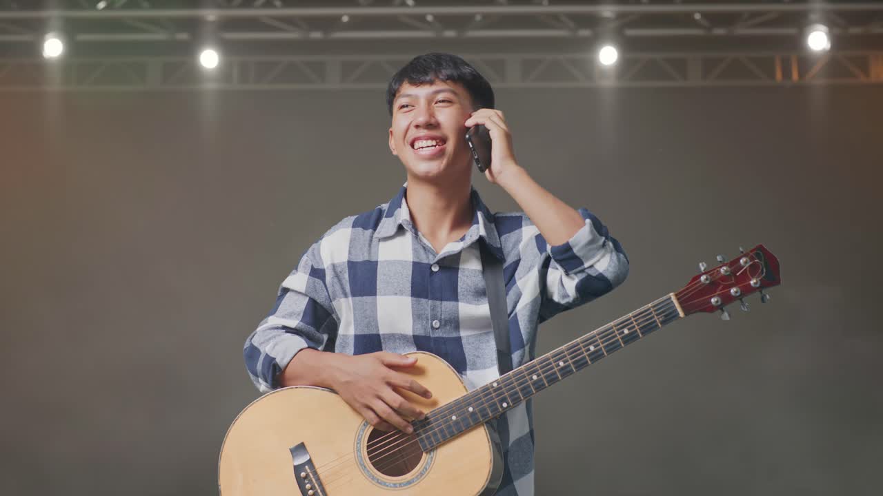 무대에 서 있는 동안 기타를 들고 스마트폰으로 대화하는 아시아 십대