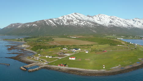 aerial view around a small village on the coast of the barents sea, snowy mountains in the background, sunny, summer day, in troms, nordland, north norway - orbit, drone shot