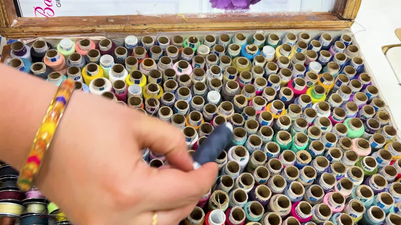 hand selecting sewing thread from organized box of colorful threads tailoring supplies close up