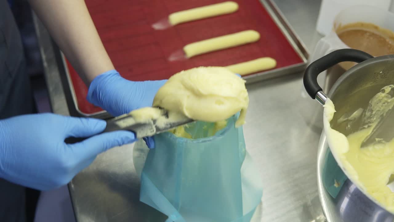 Putting brewed dough into a confectioners tube. Process of making traditional french pastry. Preparing eclaires or profiteroles.