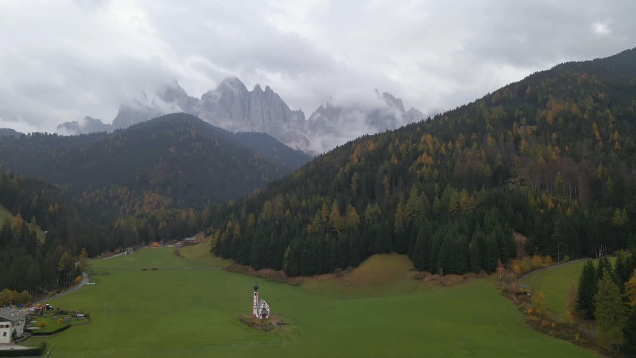 Low clouds are covering partially the Odle group peaks in the background of idyllic landscape of Santa Maddalena village in val di Funes in dolomites, during a cloudy autumn day, Italy, drone pull out