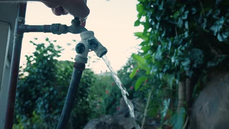 la mano de un hombre enciende una manguera exterior estacionaria con agua que comienza a fluir lentamente en cámara lenta