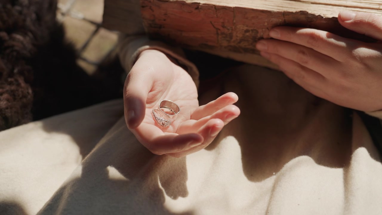 Gesù Cristo che prega con le mani giunte, in un ambiente esterno forse desertico, con la tunica, da un primo piano che si concentra sulle mani e una prospettiva superiore, con accenti marroni e bianchi.