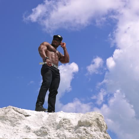 athlete man showing muscles on rocky mountain. handsome black african american man bodybuilder with naked torso posing on the rocky mountain peak