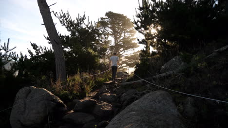 man taking hike along trail at sunrise to mountain top