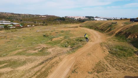 toma aérea de una pista de motocross en málaga, españa, con una pista seca y polvorienta y una colina mientras un piloto de motocross realiza un truco sobre una colina