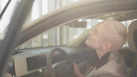 eco car sale concept. test driving of new generation electric vehicle with self driving system in showroom. attractive caucasian woman sitting behind the wheel of new modern car and smiling at camera