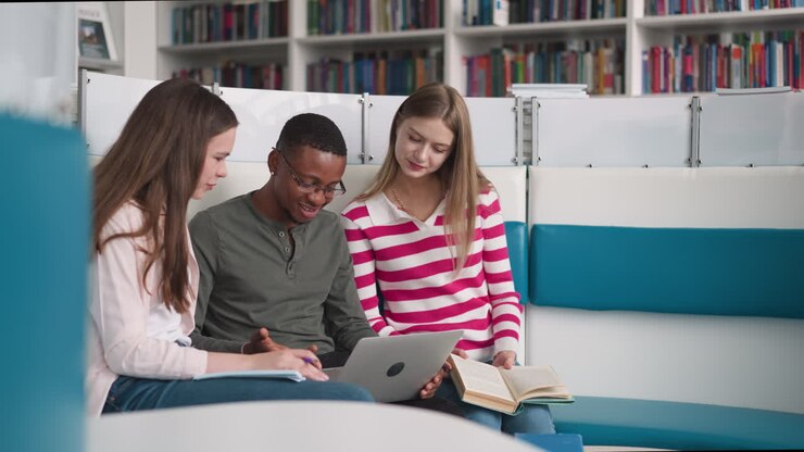 Women with black man look at laptop display in library rest zone. Positive students browse information for educative project online in reading hall