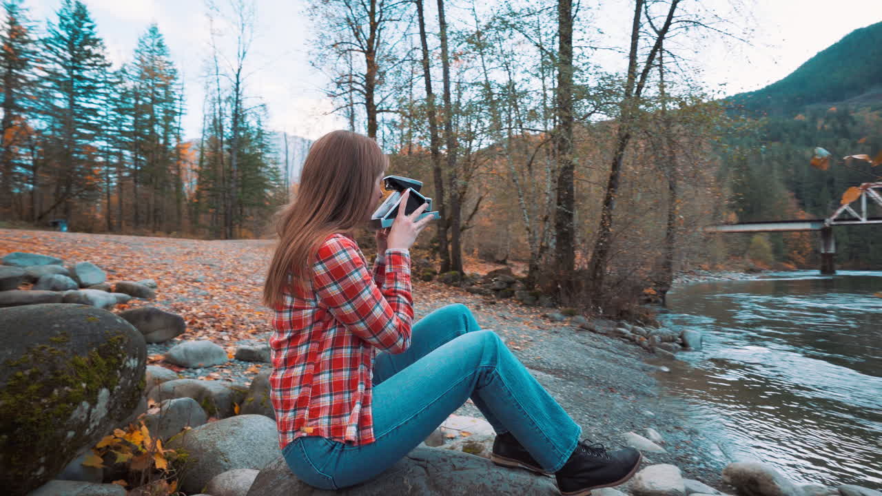 una mujer fotógrafa toma una foto polaroid a lo largo de la orilla del río entre los colores del otoño