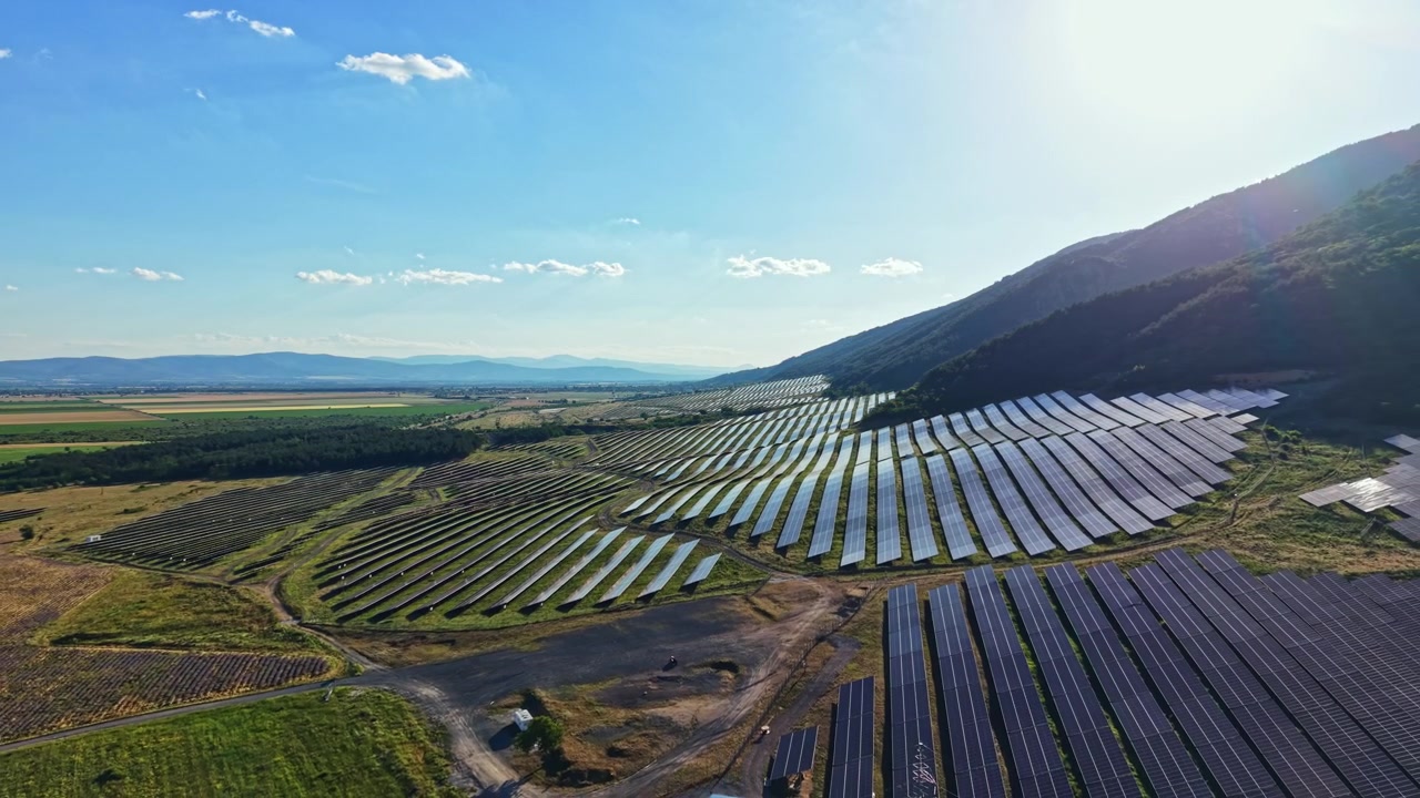 Solpaneler dækker et stort område ved foden af et bjerg under en klar blå himmel om dagen i et område med fokus på vedvarende energi.