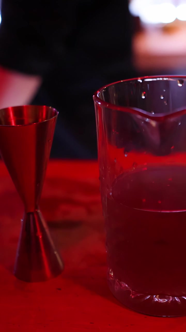 Barman prepara un cocktail usando jigger e mixing glass sotto un'illuminazione rossa suggestiva, primo piano