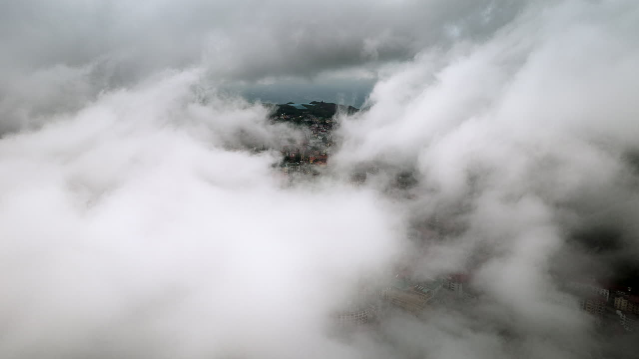 Aerial hyperlapse above Sapa city, Vietnam, with moving swirling clouds over mountain peaks and terraced fields with city buildings gradually appearing and disappearing