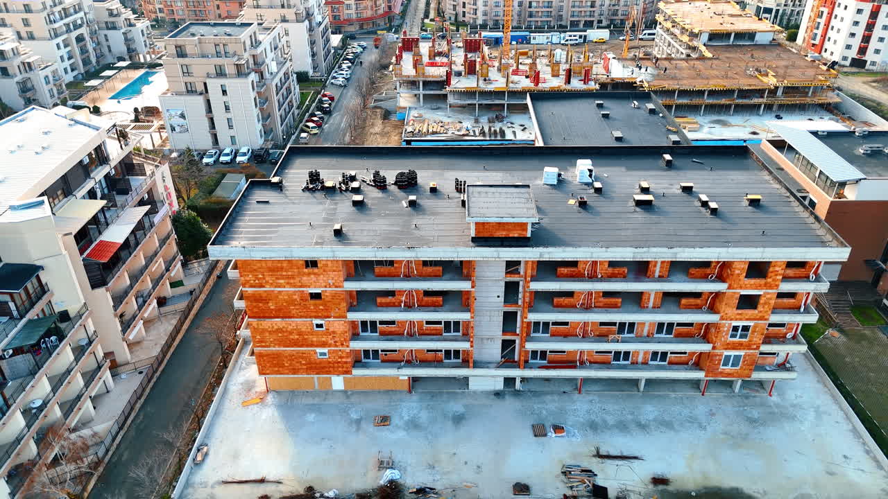 Edificio residenziale in costruzione con muri in mattoni arancioni e tetto piano. Vista dall'alto di un edificio residenziale a più piani con muratura in mattoni arancioni e un tetto scuro impermeabilizzato.