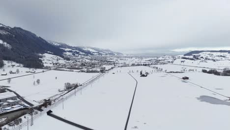 Toma-Aérea-Acercándose-Al-Paisaje-Nevado-De-Invierno-En-Suiza-Y-Montando-En-Tren-En-La-Vía