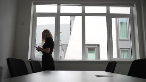 a woman in a conference room, checking her phone and pacing by the window, embodies patience and professionalism in a business environment