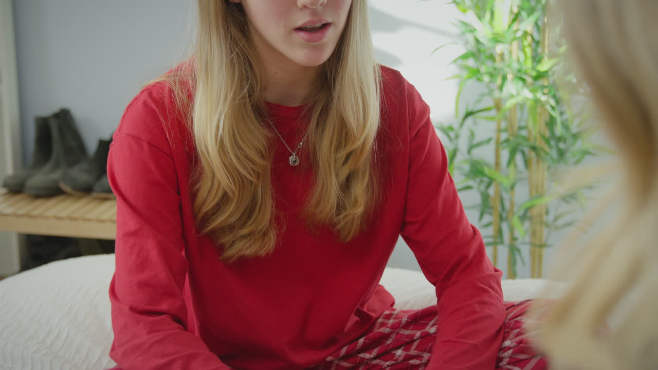 madre hablando con su hija adolescente vestida con pijama sentada en la cama en el dormitorio y sosteniendo sus manos - tomada en cámara lenta