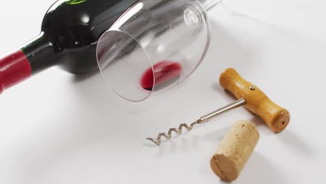 red wine bottle, empty glass, cork and corkscrew lying on white surface with copy space