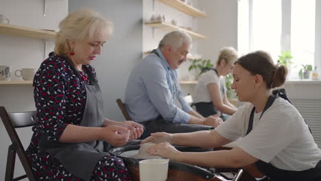 A-young-woman-conducts-a-pottery-class-for-a-group-of-senior-women-friends-and-a-man-of-60-70-years-old.-Activities-for-the-elderly