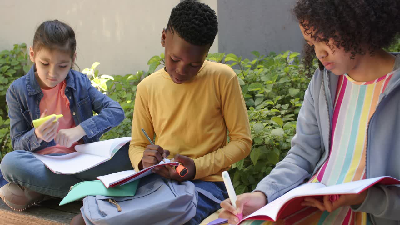 Teen students sitting on yard ledge, drawing in red pad, fixing pen, marker, writing and studying