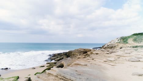 Drohne,-Die-Vom-Sandstrand-über-Felsformationen-Aufsteigt-Und-Eine-Atemberaubende-Meereslandschaft-Enthüllt