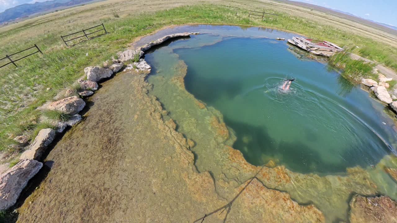Top down view of of a Hot Spring in Utah with a red haired male jumping in an swimming