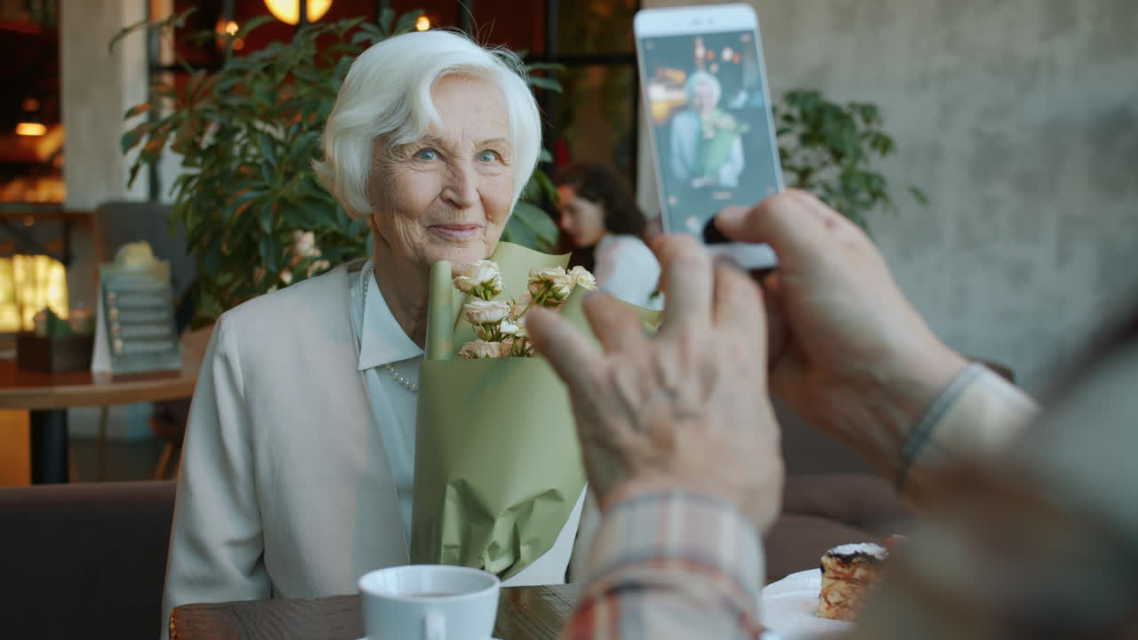 Elderly woman receiving flowers and being photographed in a cafe.