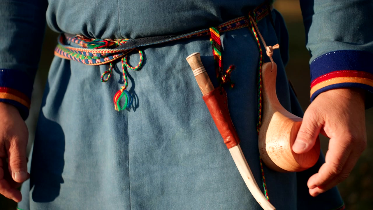 Primo piano di una persona Sami in abiti tradizionali che ripone il coltello nel suo fodero di legno