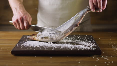 chef removes salt from herring fish with knife on board