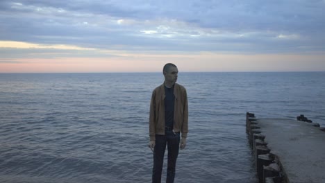 a lonely man standing at the shore while watching on his left side during sunset - wide shot