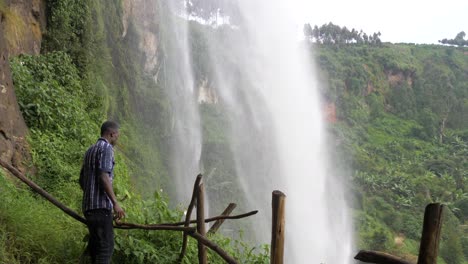 hombre africano parado detrás de una cascada tropical mirando con asombro