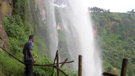 african man standing behind a tropical waterfall looking up in awe