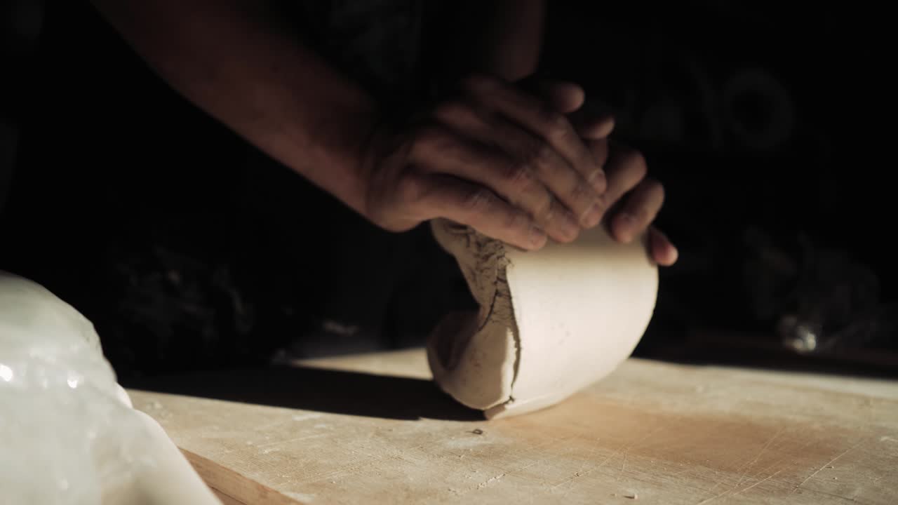 las manos de los hombres están amassando arcilla en la mesa en un rayo de luz solar.